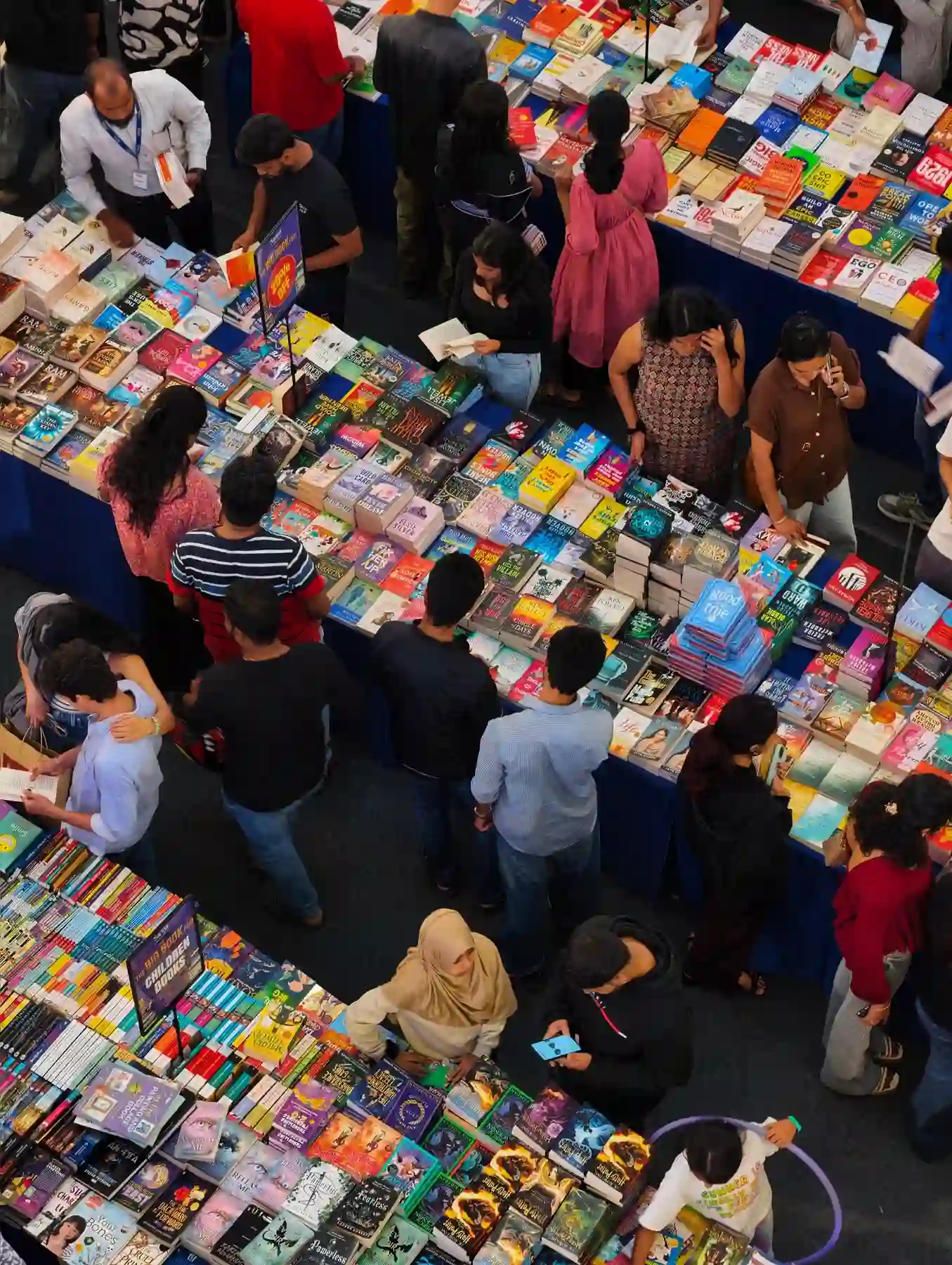 An aerial view of a busy book fair table, readers browsing stacks of titles
