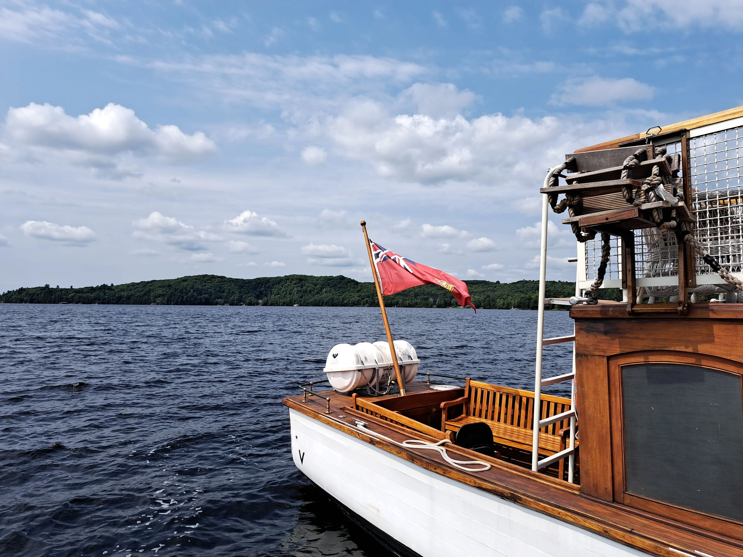 A classic wooden Muskoka launch boat with a red ensign flag, out on the water near Baysville