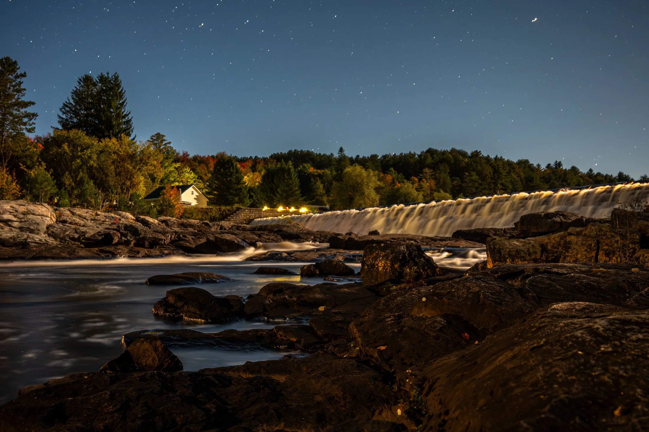 Bracebridge Falls lit up at night, with the town reflected in the water