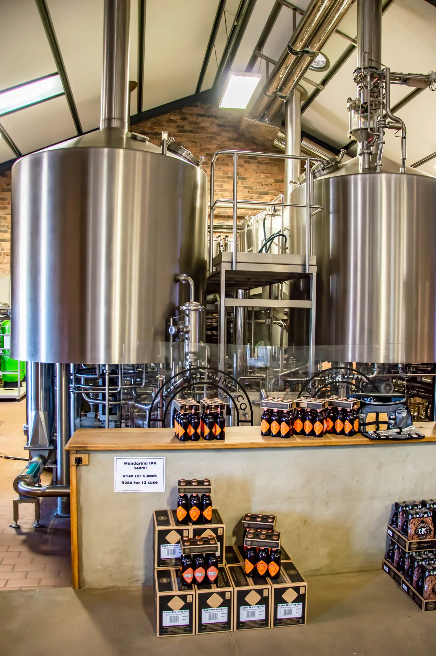 Brewing tanks behind a counter stacked with packaged beer