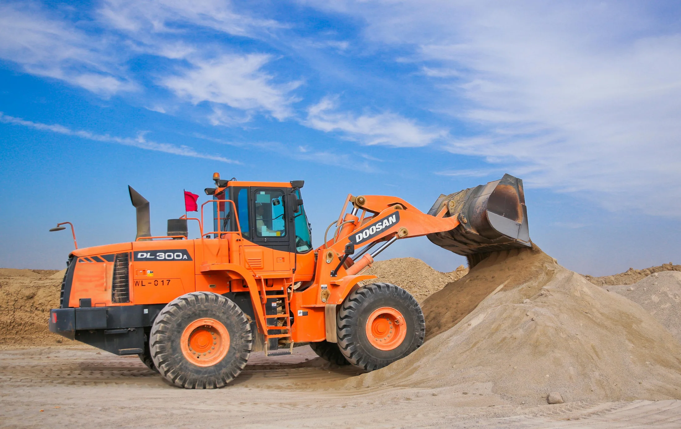 An orange wheel loader moving material against a bright blue sky