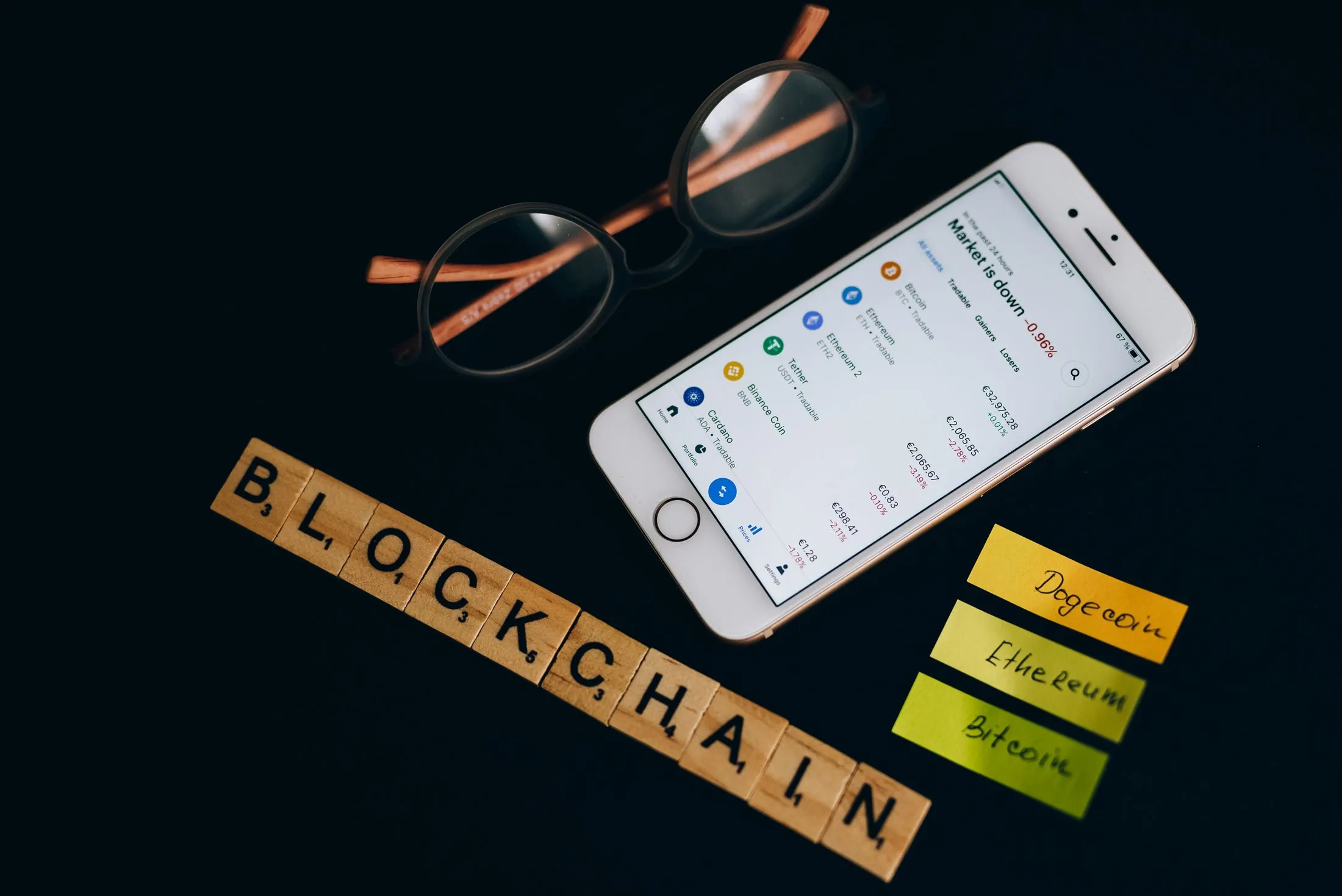 A phone showing crypto market data beside letter tiles spelling 'blockchain'