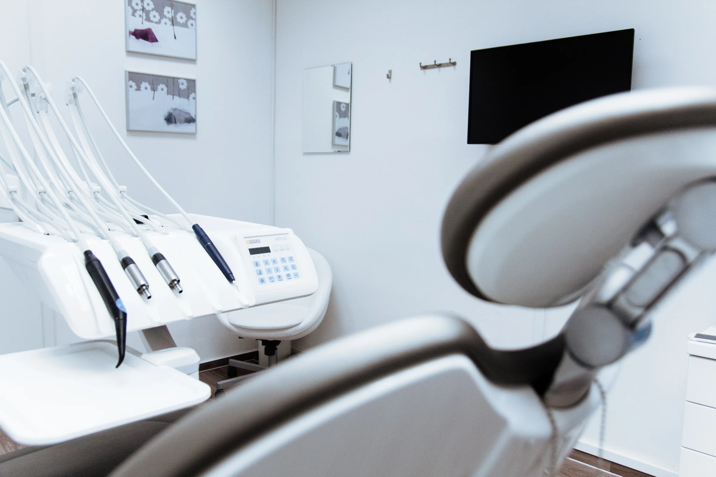 A calm, modern dental treatment room with framed art and a wall-mounted TV