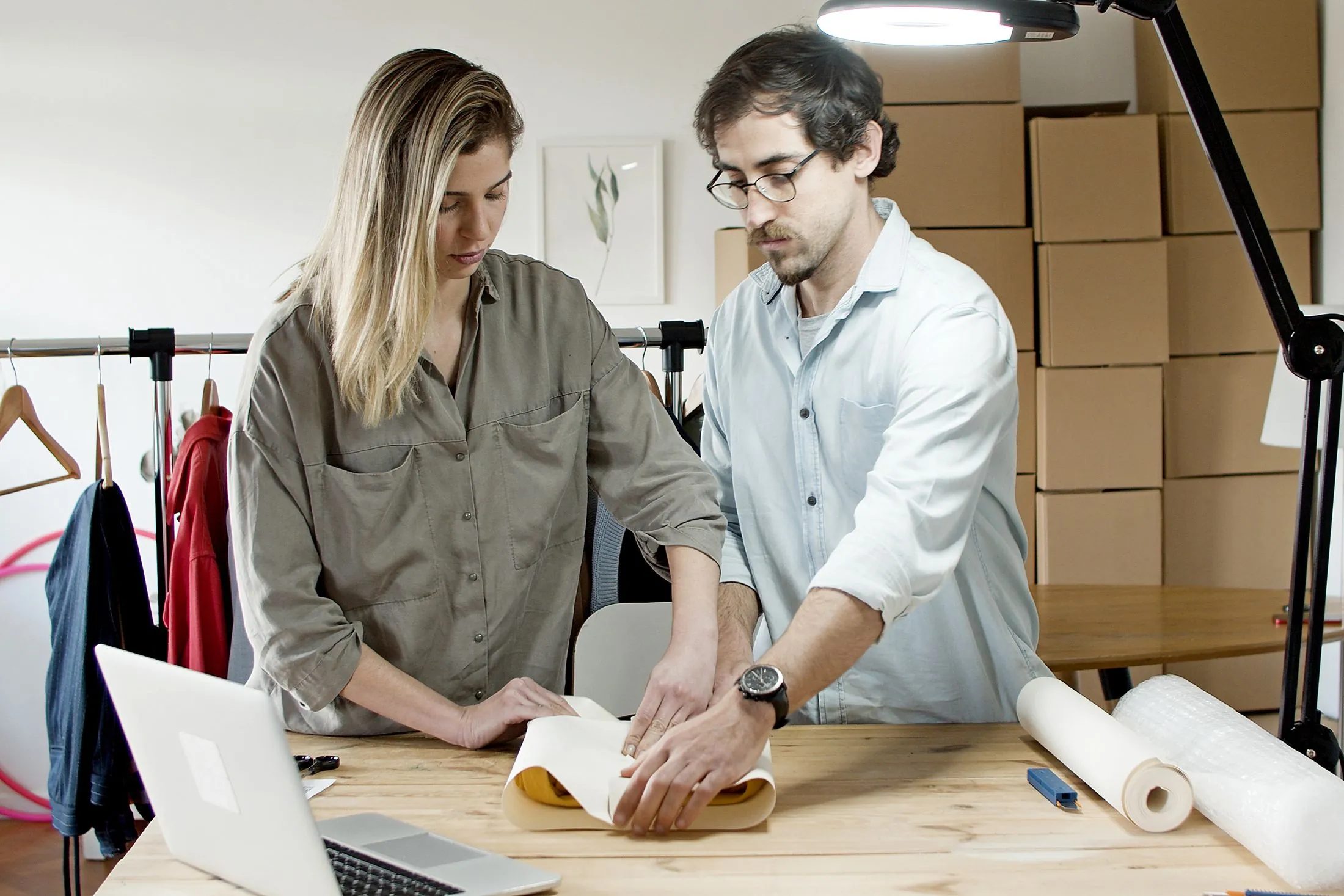 Two people wrapping products for shipping at a worktable with a laptop