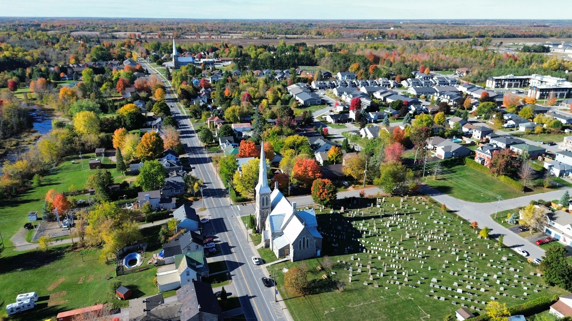 Aerial view of a village church and cemetery surrounded by autumn trees and new homes