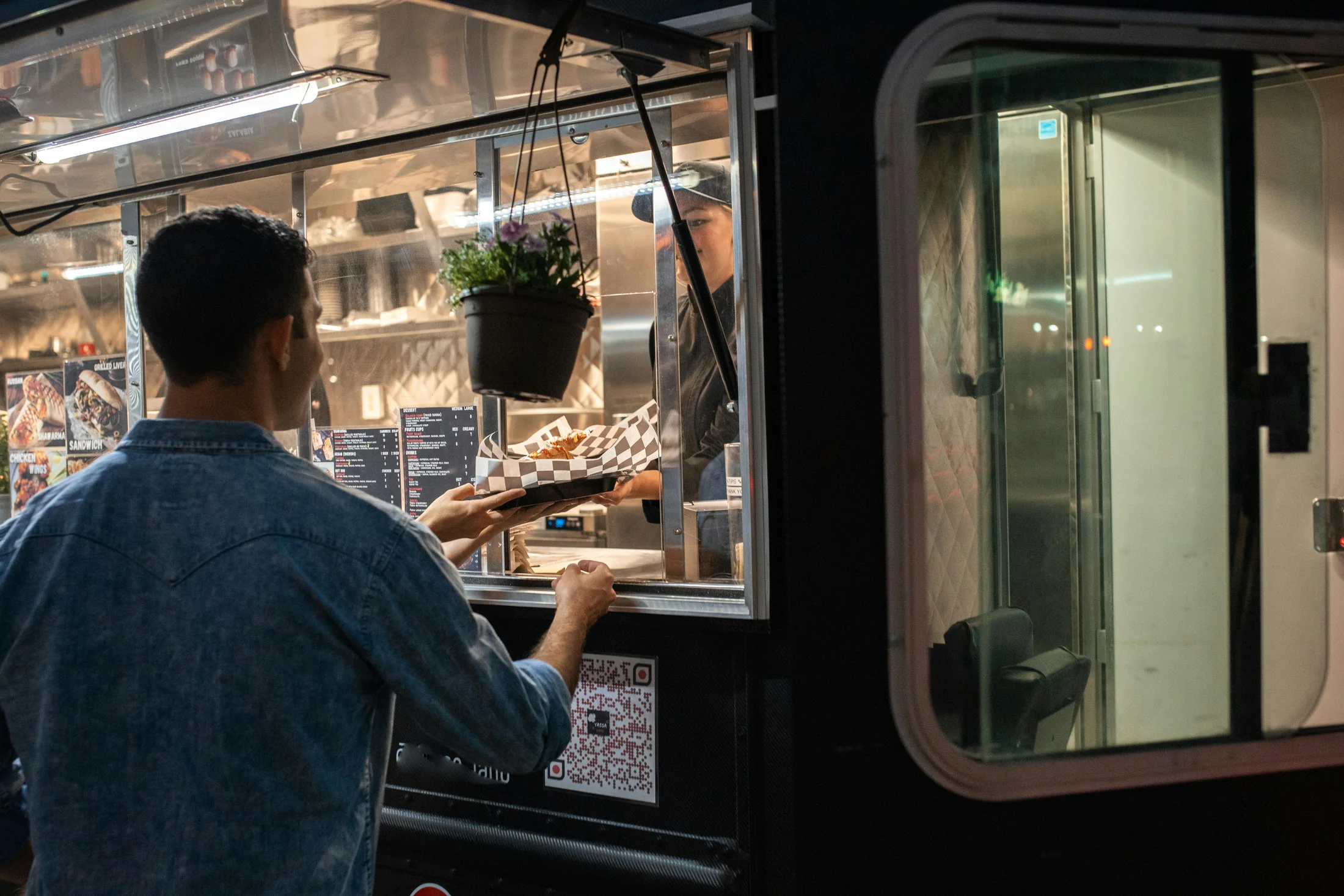 A food truck vendor handing a customer their order through the service window