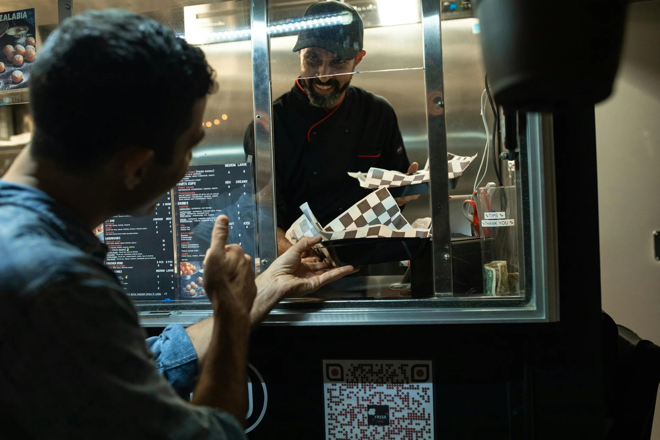 A smiling food truck chef handing over an order in checkered paper