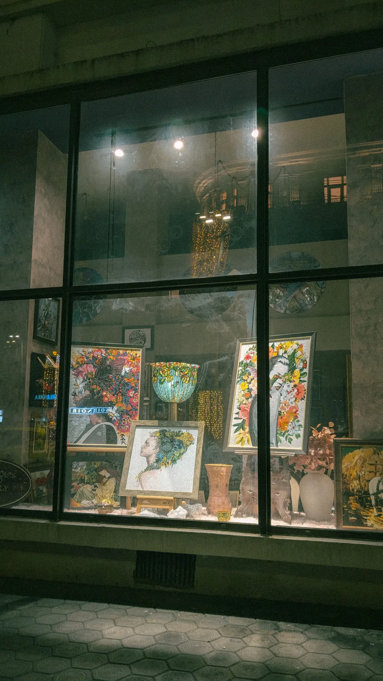 Paintings and ceramics glowing in a shop window at night