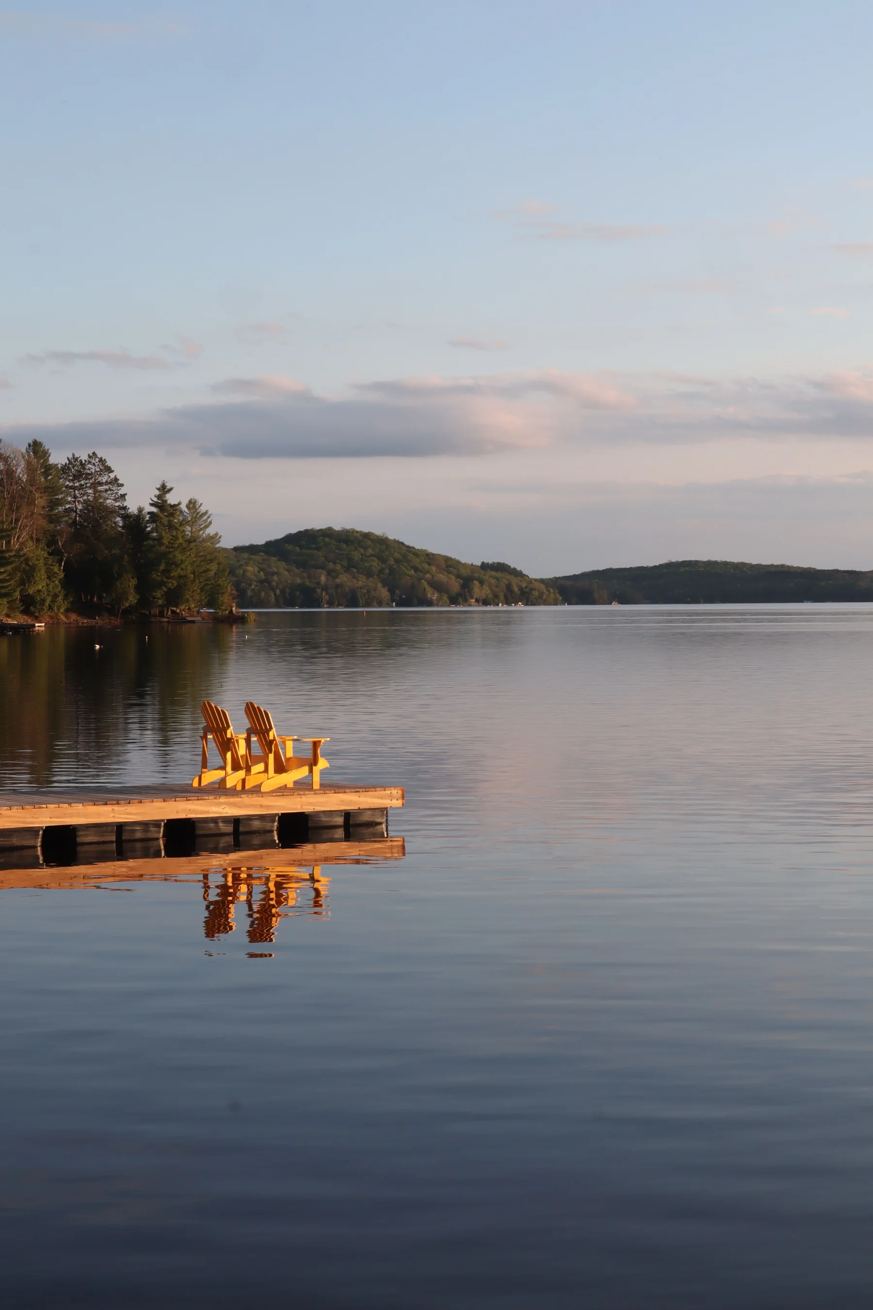 Two yellow Muskoka chairs on a dock at sunset near Huntsville