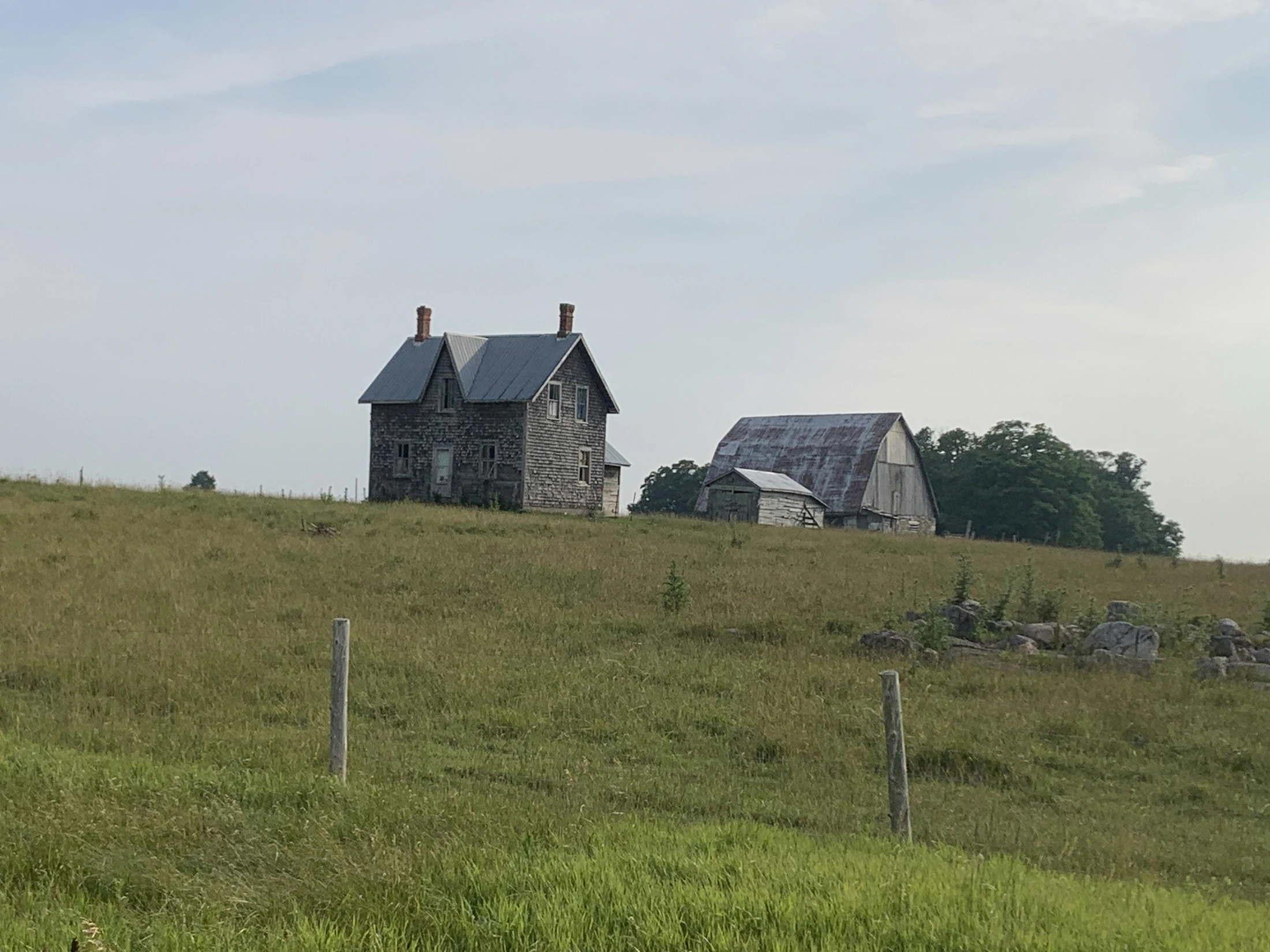 An old farmhouse and barn on a rolling green hill