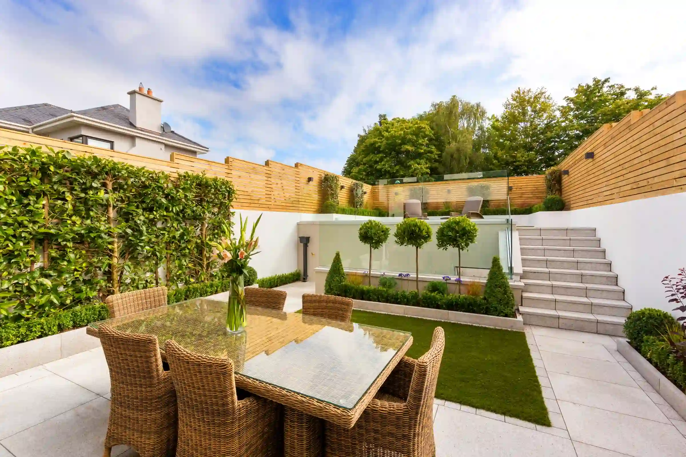 A finished backyard landscaping project with a stone patio, dining set and manicured hedges