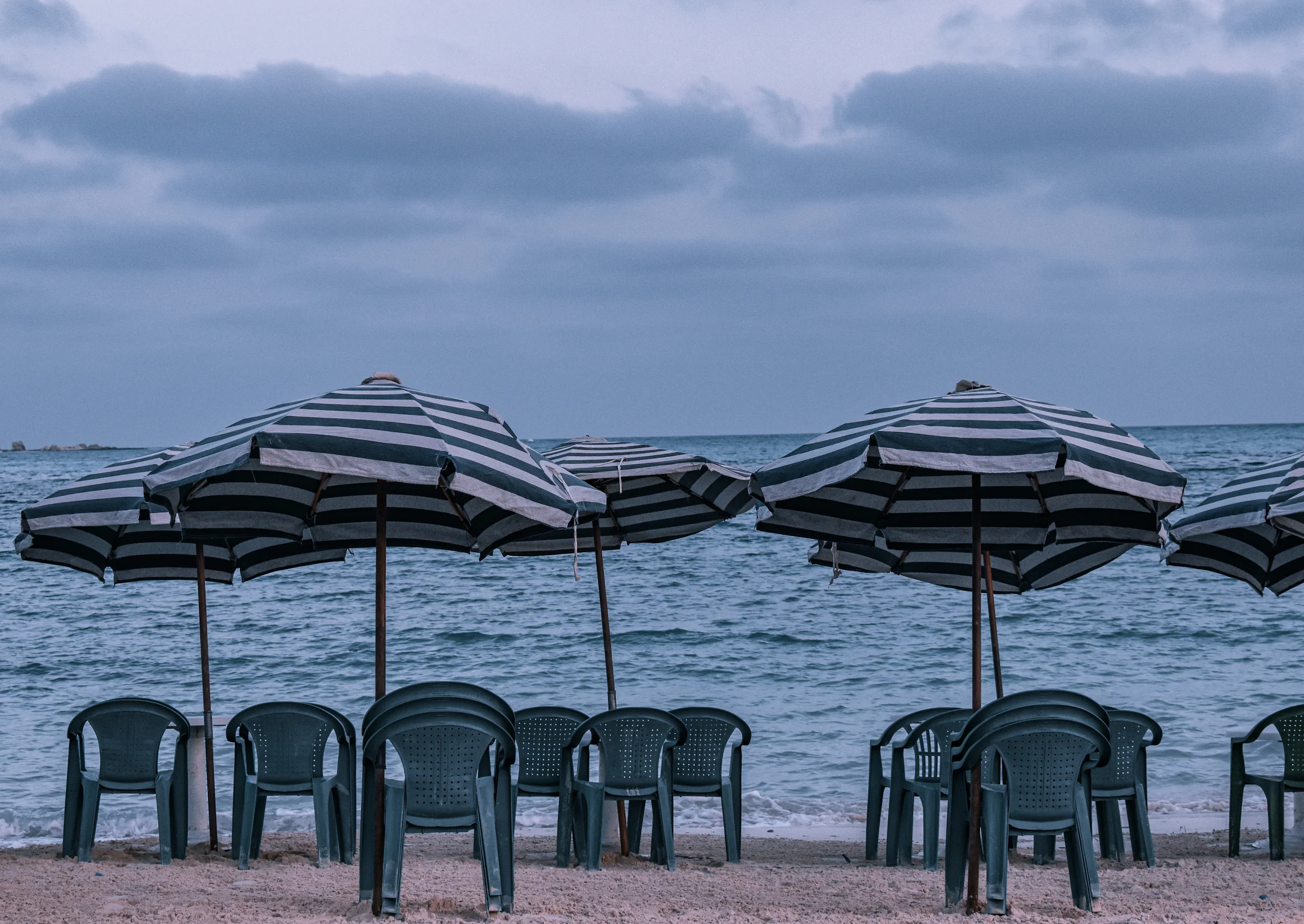 Striped beach umbrellas and chairs lined up facing the water at dusk
