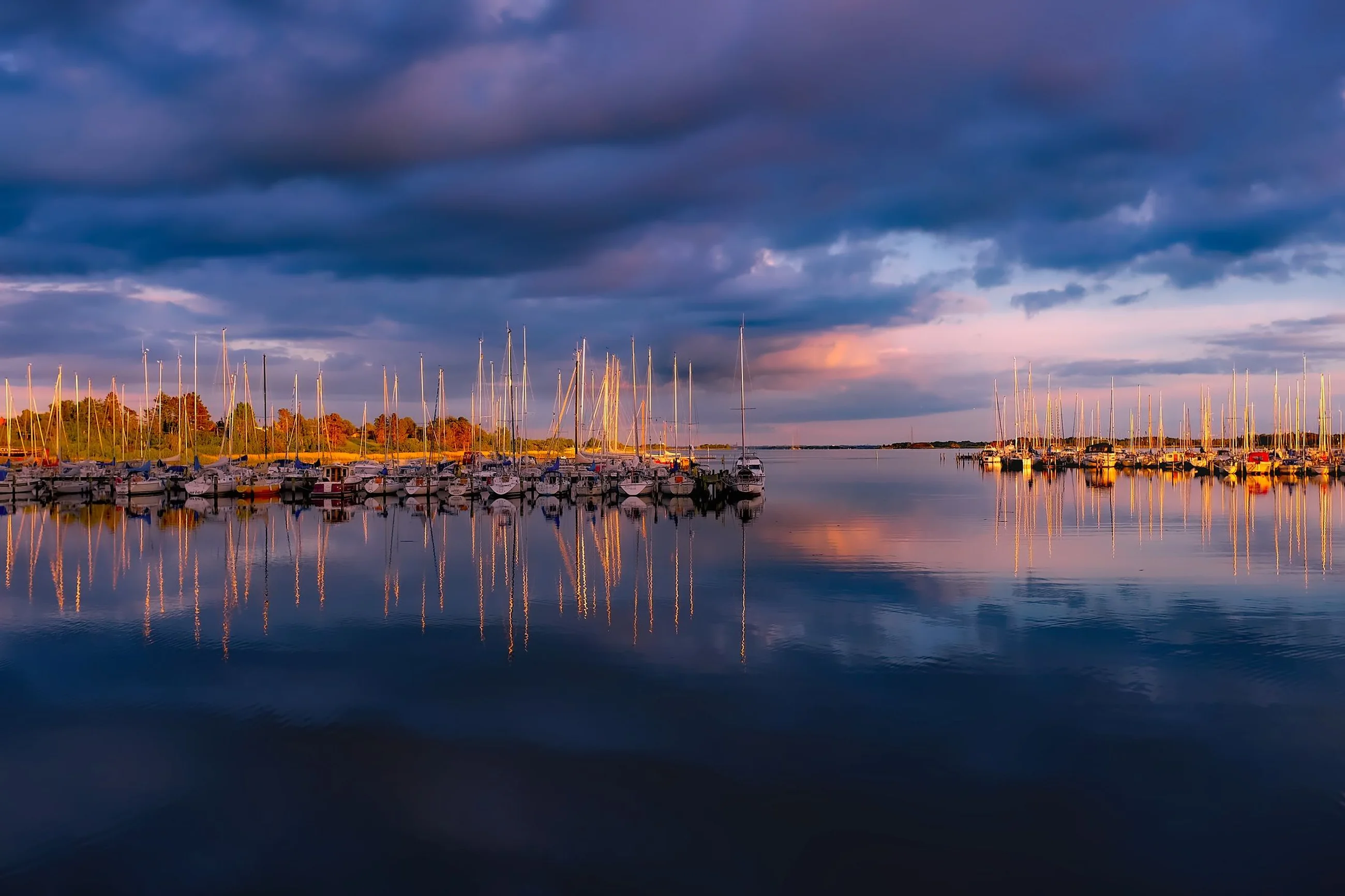 A marina full of sailboats reflected in still water at dusk