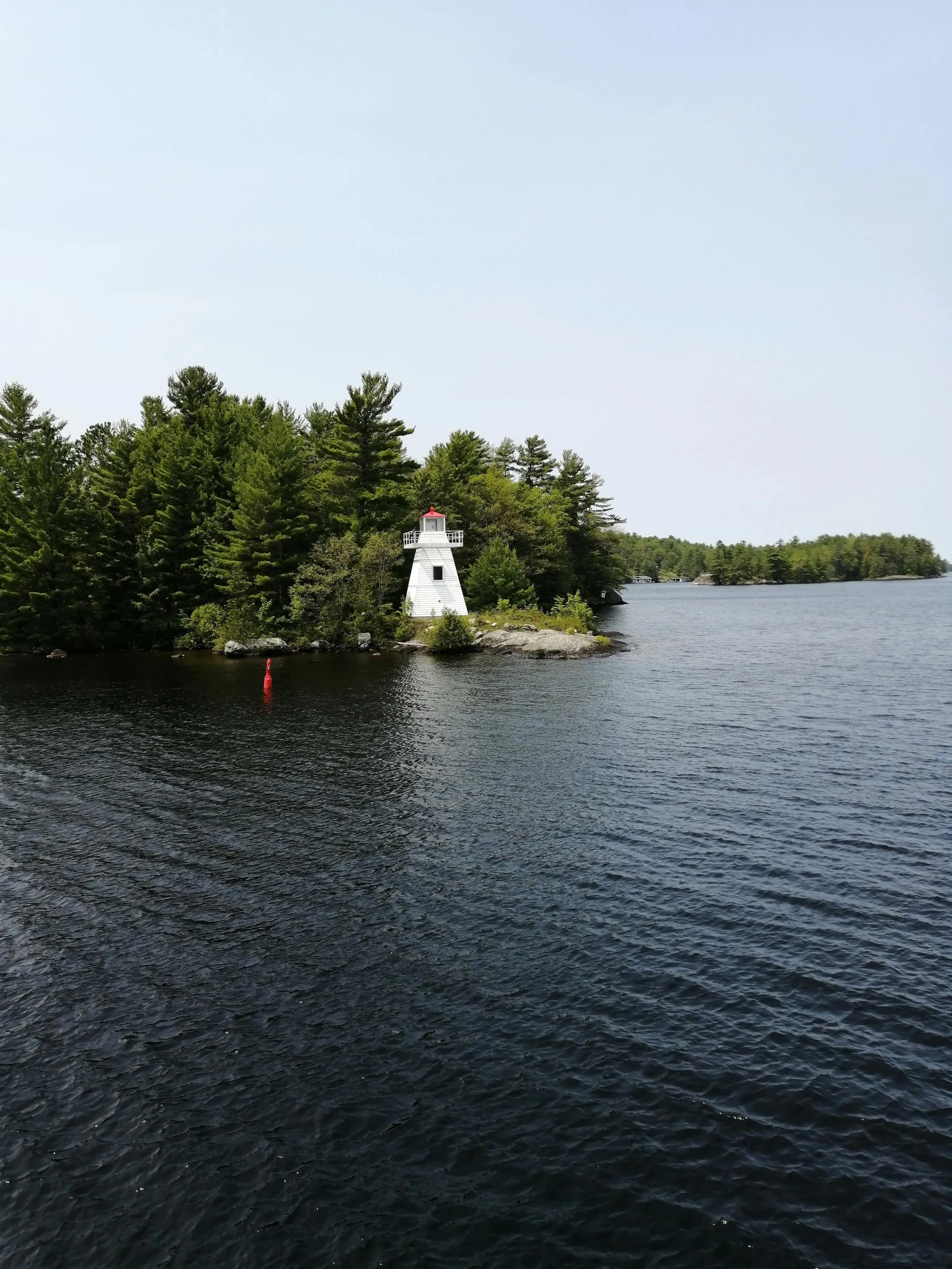 A small white lighthouse on a wooded island in calm water