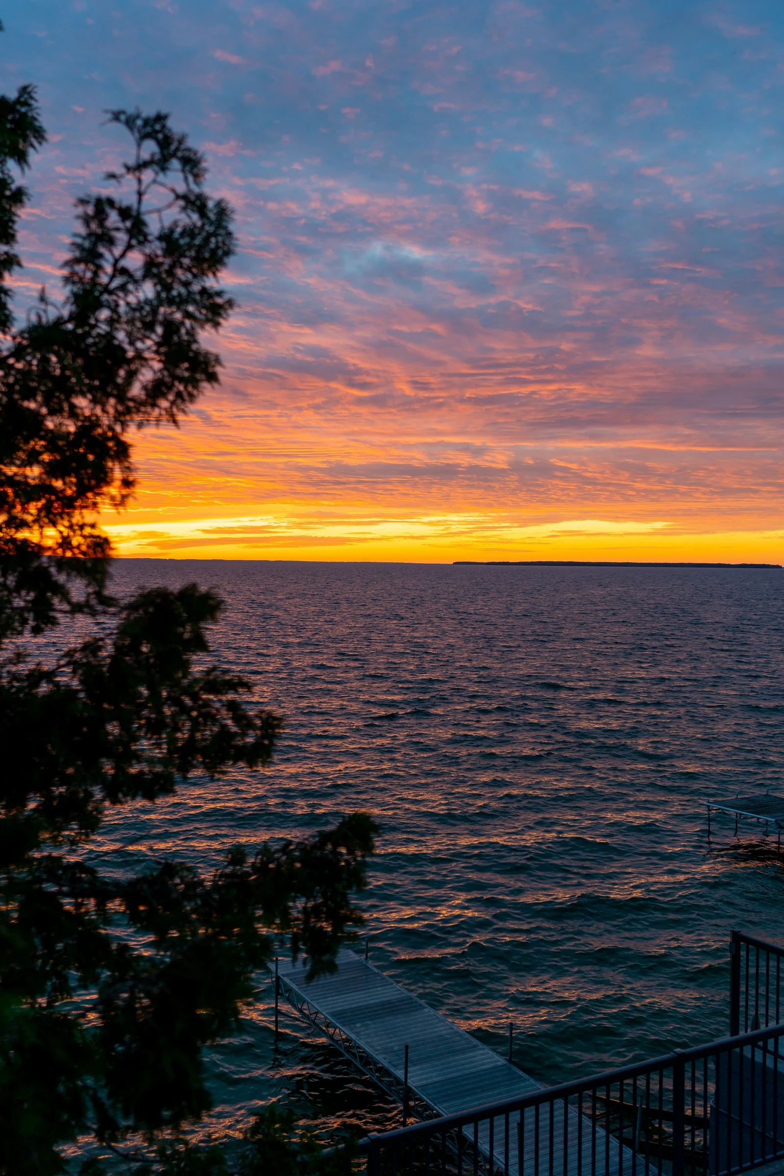 A wooden dock at sunset, with orange and pink sky over the water