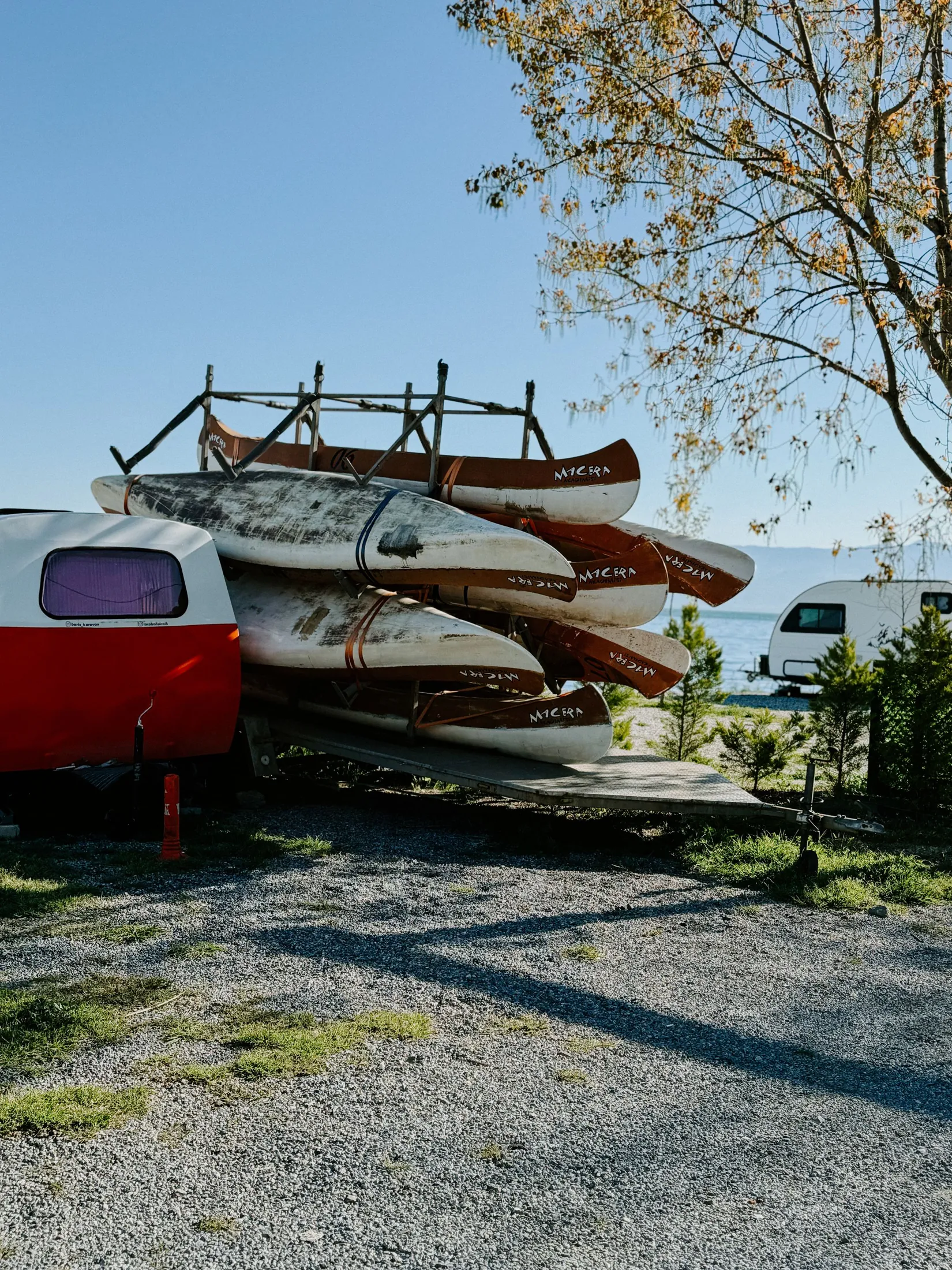 Canoes stacked on a rack beside a red camper at a lakeside camp