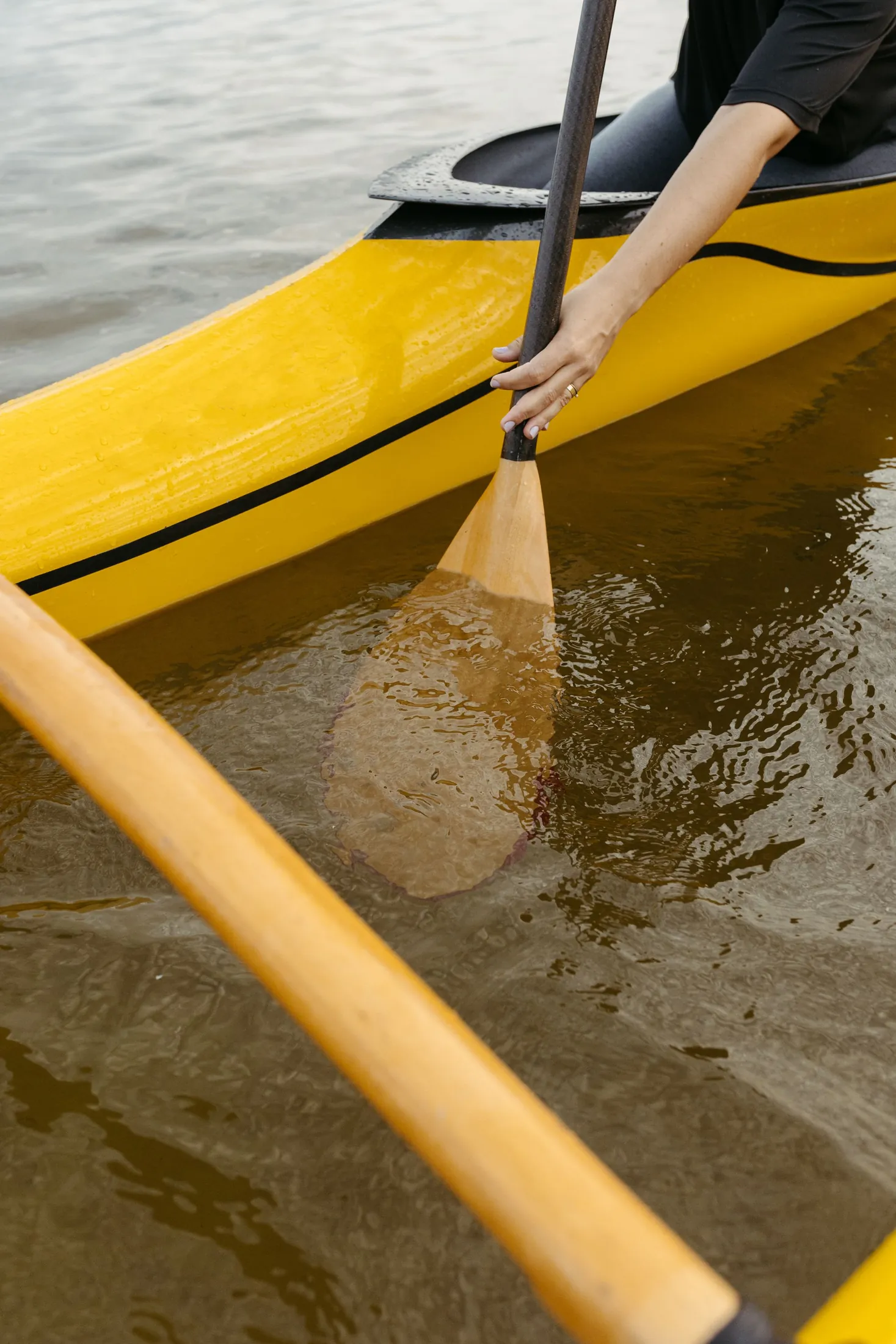 A paddle dipping into calm water beside a yellow canoe