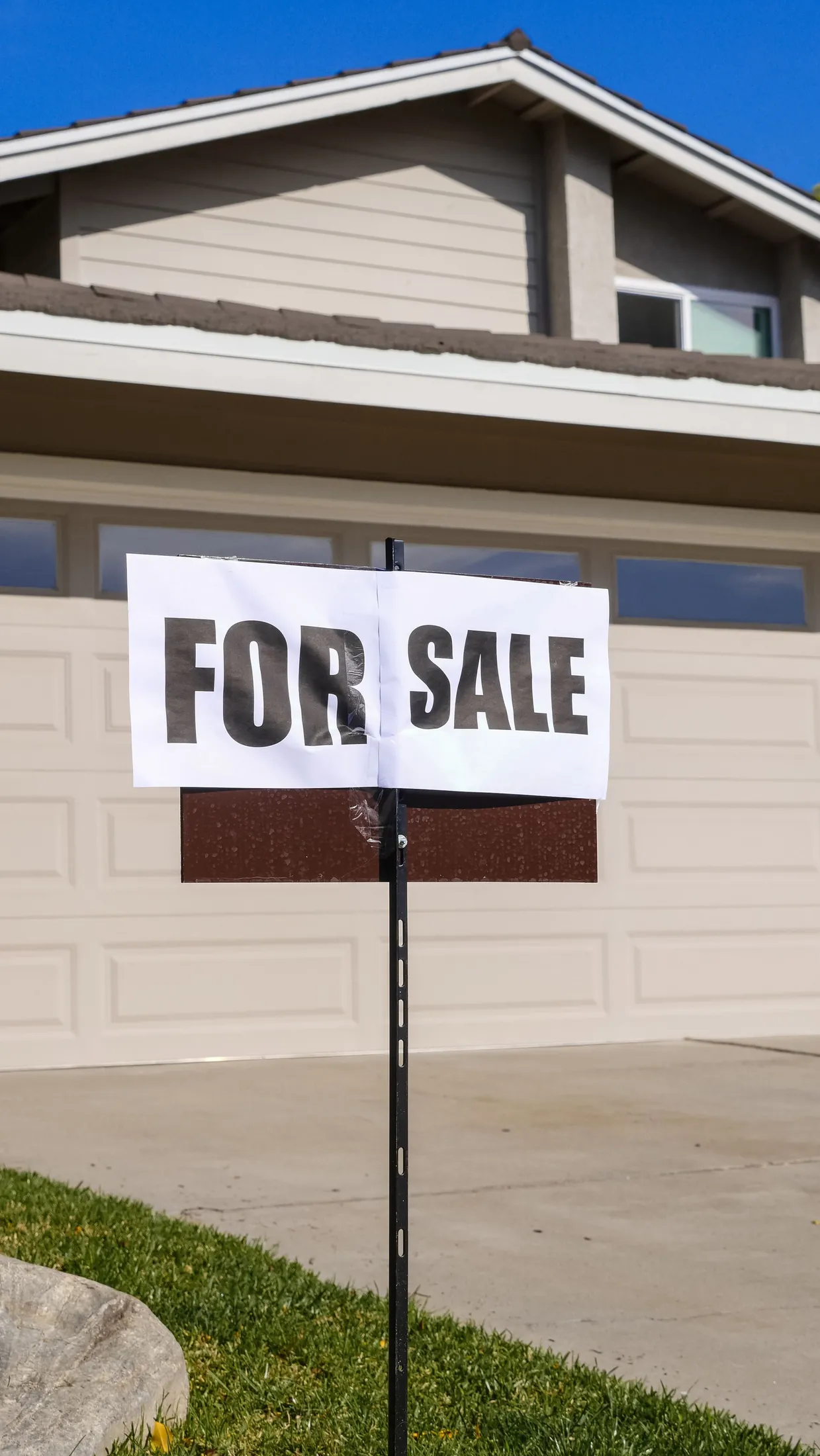 A 'For Sale' sign in front of a suburban house
