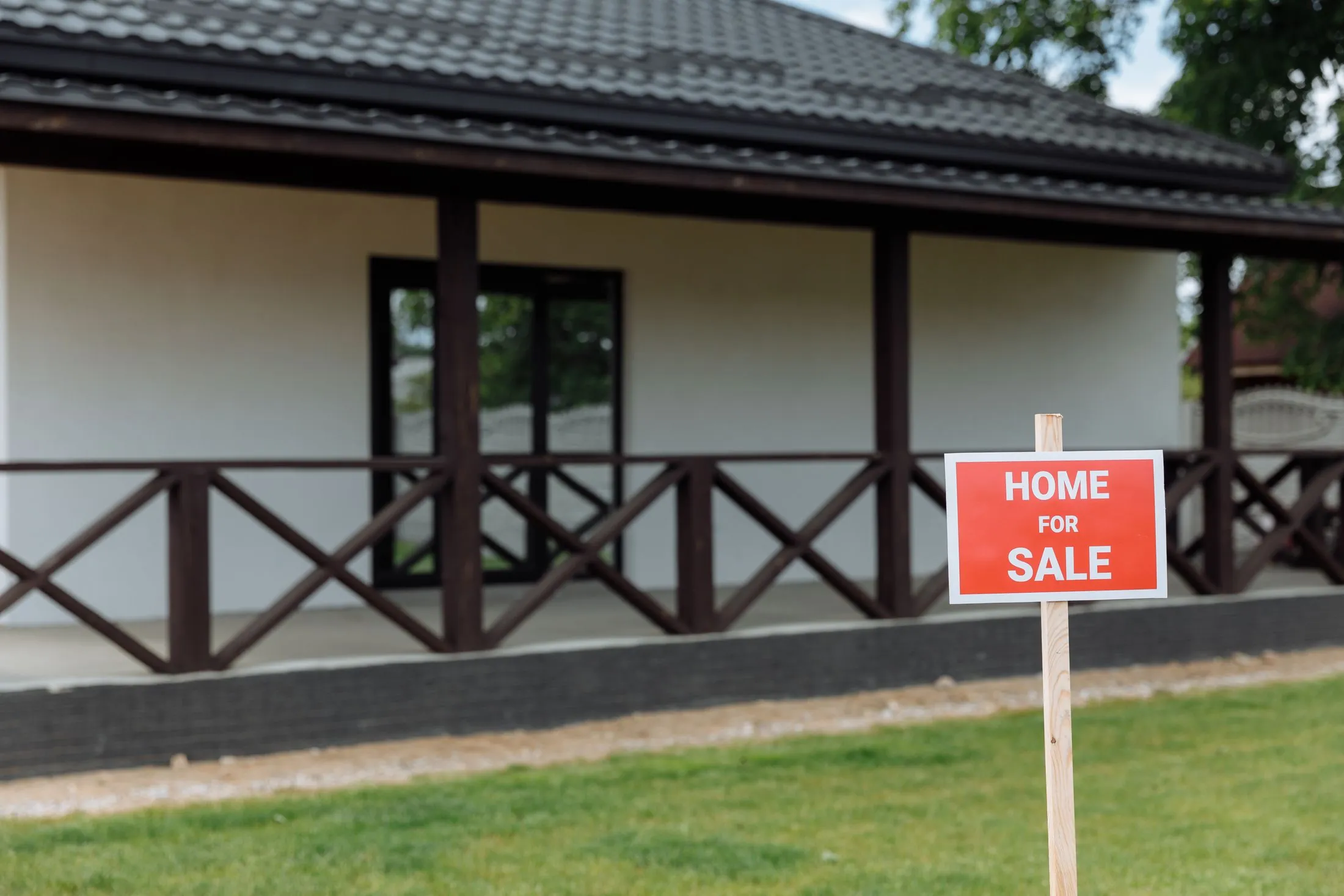 A house with a wide porch and a red 'Home for sale' sign on the lawn