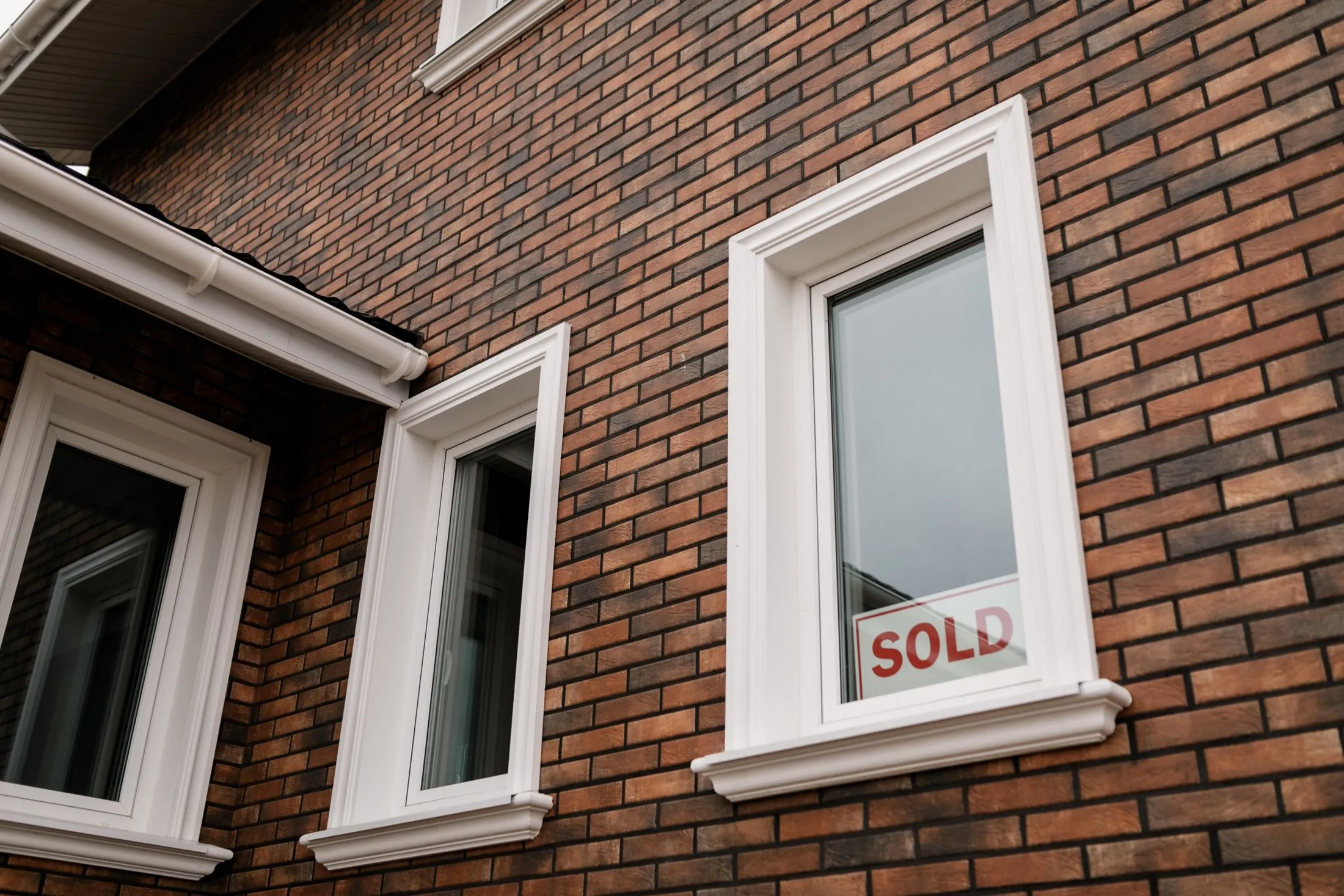 A brick house with a 'Sold' sign in the window