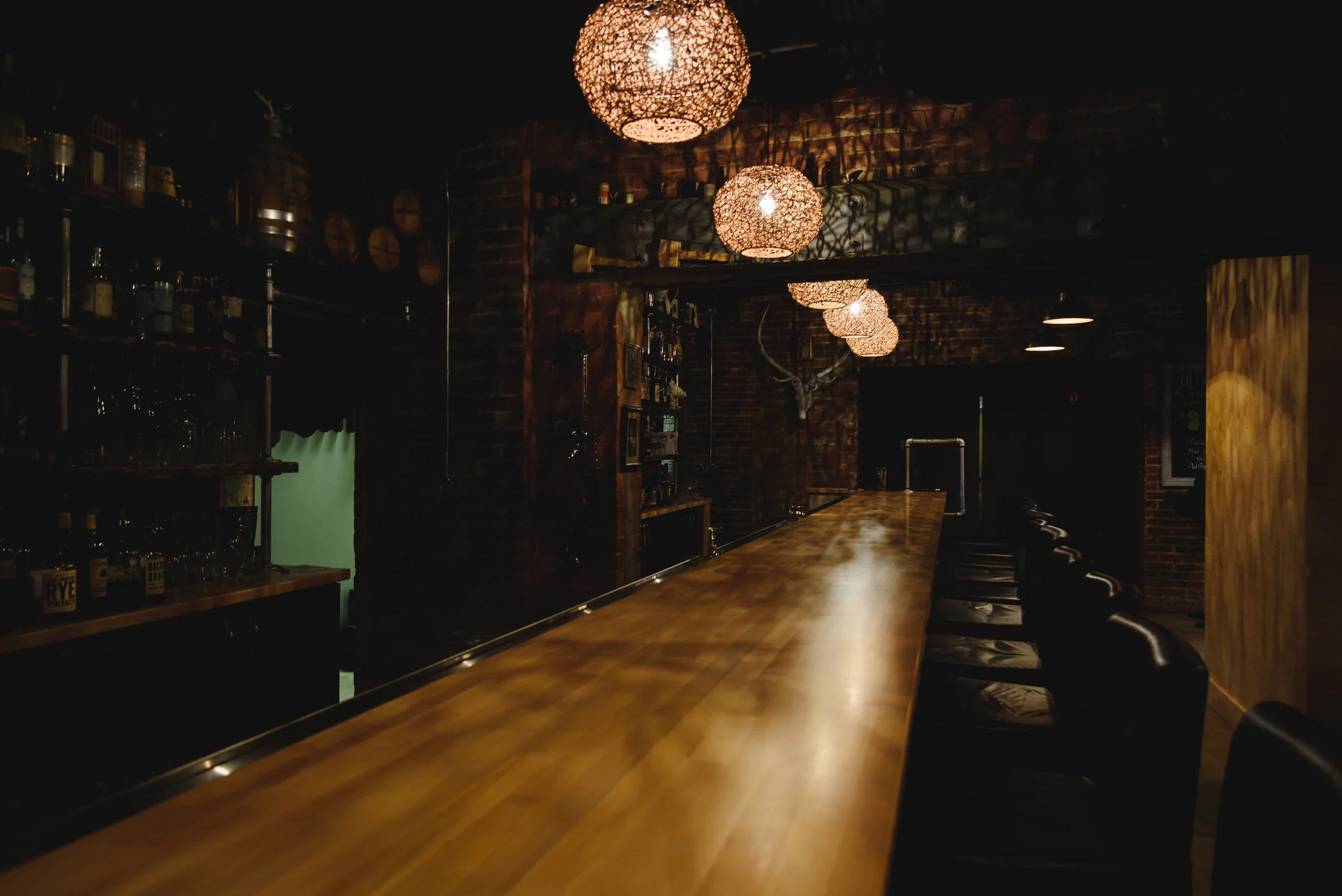 A long wooden bar lined with bottles under warm hanging lights