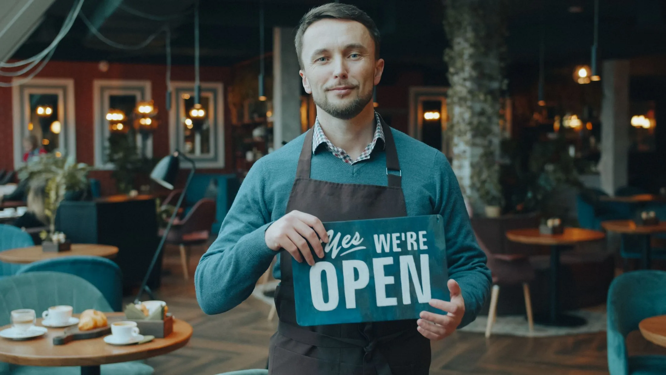 A cafe owner holding a 'Yes, we're open' sign inside the cafe